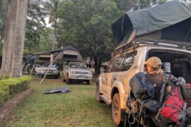 Travelers preparing for a self-drive camping safari with Toyota Land Cruisers fitted with rooftop tents at a scenic campsite in Uganda.