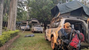 Travelers preparing for a self-drive camping safari with Toyota Land Cruisers fitted with rooftop tents at a scenic campsite in Uganda.